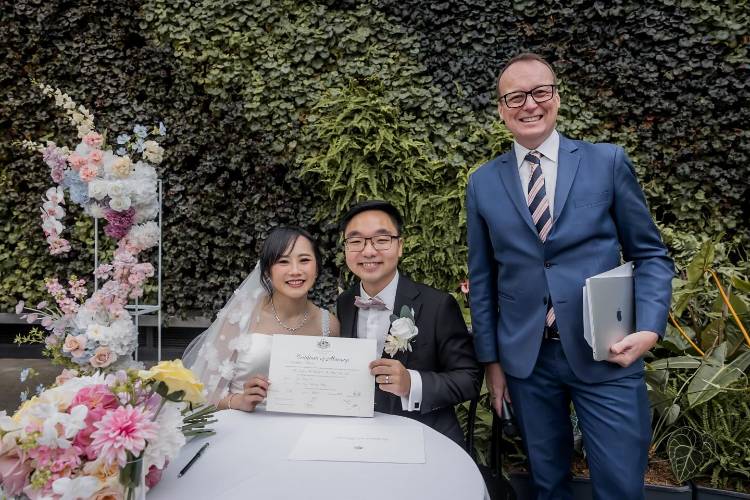 Refined male celebrant Chris Stedman with newlyweds holding marriage certificate